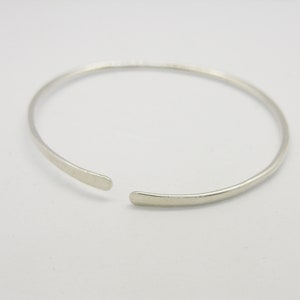 May include: A simple silver bangle bracelet with a slightly open design.