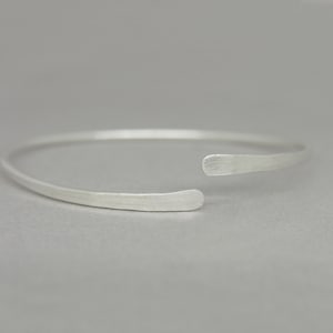 May include: A simple silver bangle bracelet with a slightly curved, open design.