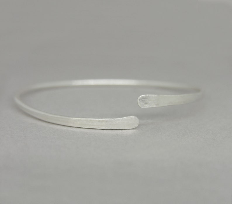 May include: A simple silver bangle bracelet with a slightly curved, open design.