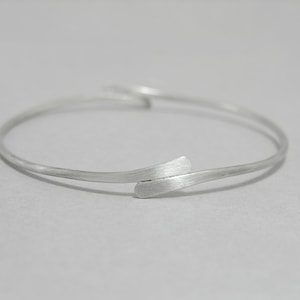 May include: A silver bangle bracelet with a unique, twisted design. The bracelet is made of a single piece of metal that is bent and twisted to create a unique and modern look.