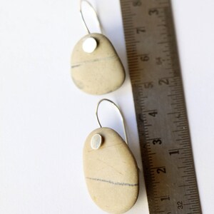 May include: A pair of silver dangle earrings with a natural stone pendant. Each stone is a different shape and has a silver accent. The earrings are shown next to a ruler for size reference.
