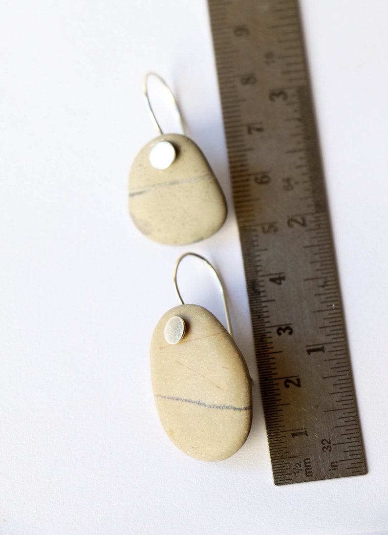 May include: A pair of silver dangle earrings with a natural stone pendant. Each stone is a different shape and has a silver accent. The earrings are shown next to a ruler for size reference.