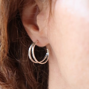 Op de afbeelding: Een paar zilveren creolen met een gehamerde textuur. De oorbellen worden in het oor van een persoon gedragen.