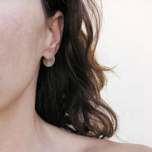 May include: A close-up of a person's ear with a silver disc earring. The earring is textured and has a slightly curved shape.