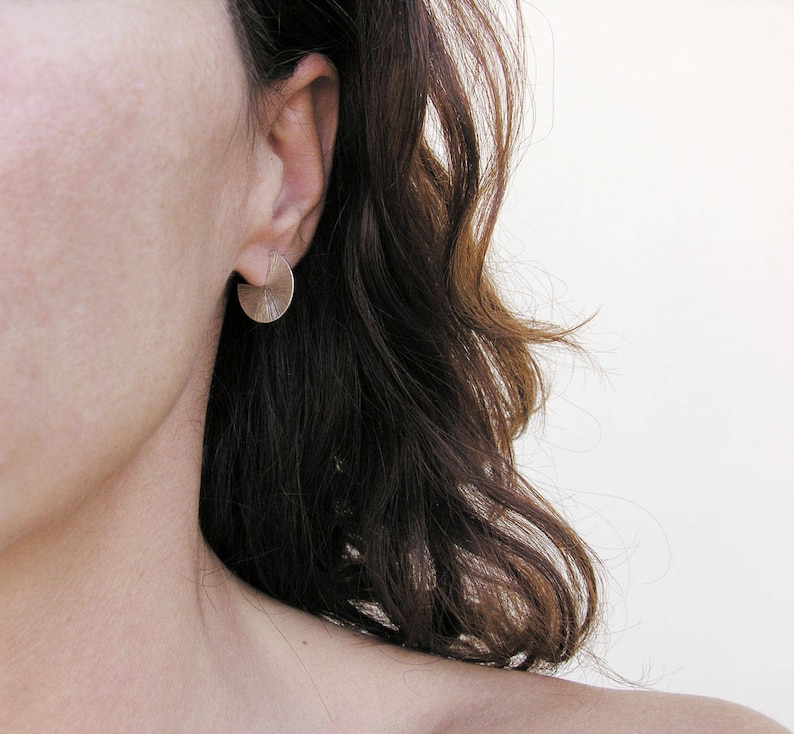 May include: A close-up of a person's ear with a silver disc earring. The earring is textured and has a slightly curved shape.