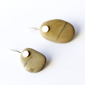 May include: A pair of silver earrings with a small white circle attached to a brown stone. The stones are oval shaped and have a natural, rough texture.