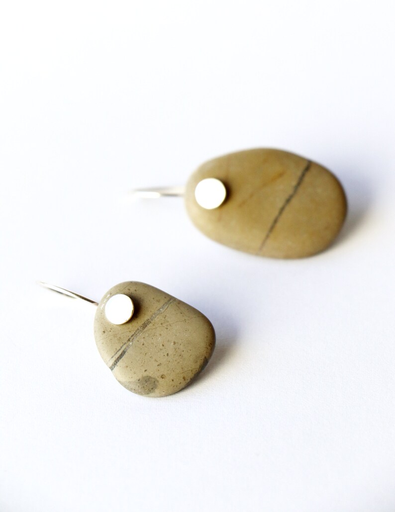 May include: A pair of silver earrings with a small white circle attached to a brown stone. The stones are oval shaped and have a natural, rough texture.