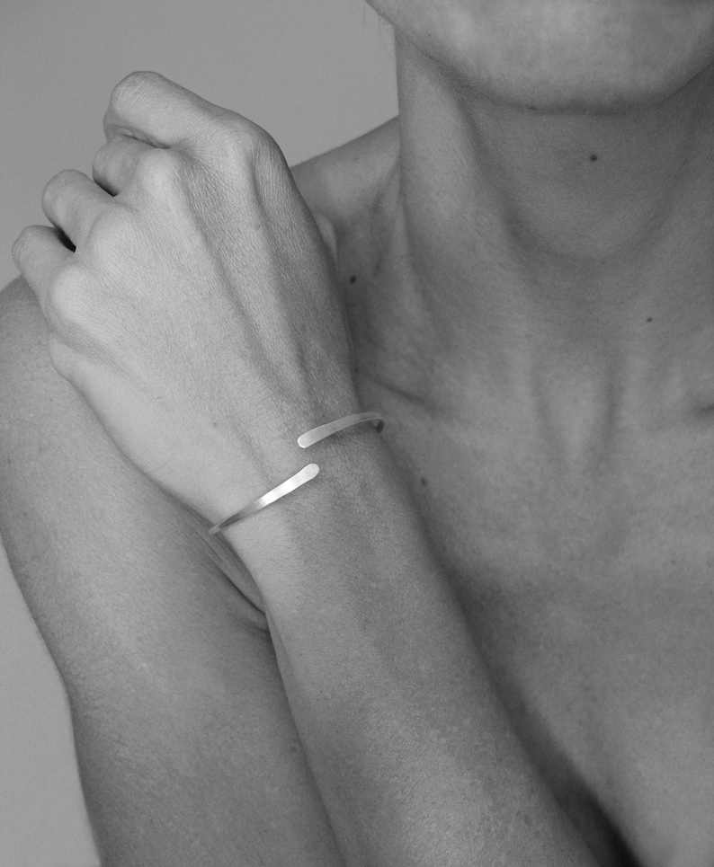 May include: A silver bracelet with a simple, open design. The bracelet is made of two thin, curved pieces of metal that intersect in the middle.