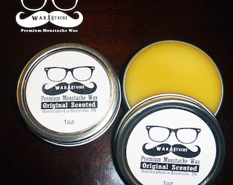 May include: Two round metal tins with white labels and black text. The labels feature a pair of glasses with a mustache and the text "WAXASTACHE Premium Moustache Wax Original Scented Handcrafted in Knoxville, TN 1oz."