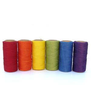 May include: Six spools of thread in rainbow colors: red, orange, yellow, green, blue, and purple. The spools are arranged in a row from left to right.