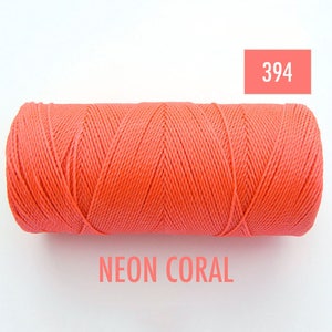 Puede incluir: Una bobina de hilo de color coral neón. La bobina está etiquetada con el número 394 y las palabras "NEON CORAL".