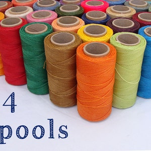 May include: A collection of 54 spools of colourful thread, arranged in a row on a white surface. The spools are made of wood and have a variety of colours, including red, orange, yellow, green, blue, and purple.