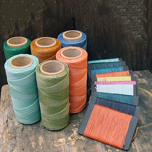 May include: A collection of spools of colorful thread, including green, orange, blue, and teal, arranged on a wooden surface. The spools are wrapped in different colors of thread, and some are stacked on top of each other.
