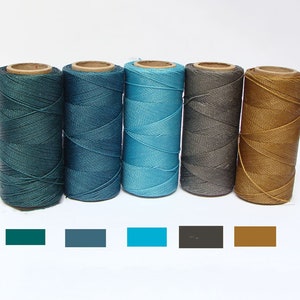 Può includere: Cinque bobine di filo cerato in varie tonalità di blu, grigio e marrone. Il filo è avvolto strettamente sulle bobine, che sono fatte di cartone.