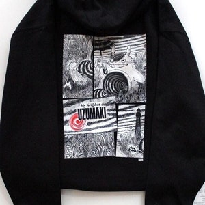 Puede incluir: Sudadera con capucha negra con un estampado gráfico de un panel de cómic con un personaje de la serie de manga "Uzumaki" de Junji Ito. El texto "My Neighbor Uzumaki" está impreso en el gráfico.