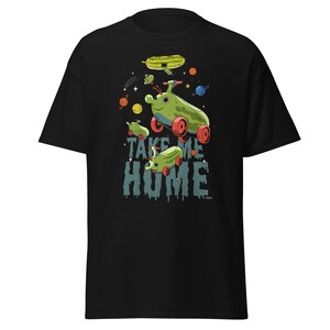 Peut inclure: T-shirt noir avec un motif fantaisiste de v&eacute;hicules verts en forme de concombre avec des roues rouges, sur fond spatial. L'inscription "TAKE ME HOME" est imprim&eacute;e en dessous. Des plan&egrave;tes et des &eacute;toiles sont &eacute;galement visibles.