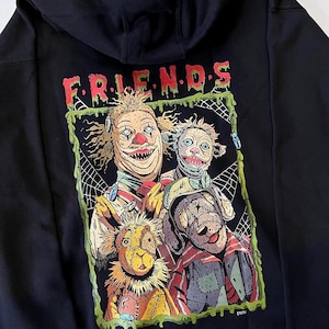 Puede incluir: Sudadera con capucha negra con un gráfico de cuatro personajes inquietantes, incluyendo un payaso y un conejo, con la palabra "FRIENDS" en letras goteantes verdes y rojas. Los personajes tienen expresiones perturbadoras.