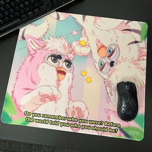 Puede incluir: Alfombrilla de ratón rectangular con una colorida ilustración de dos criaturas estilizadas con ojos grandes y pelaje. La alfombrilla tiene un fondo de arcoíris pastel con el texto "Do you remember who you were? Before the world told you who you should be?"
