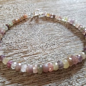 Puede incluir: Un delicado brazalete hecho con pequeñas piedras preciosas facetadas en tonos de rosa, blanco y verde. El brazalete está enhebrado en una cadena de plata y tiene un cierre simple.