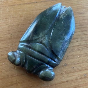 May include: A carved, dark green jade pendant. The jade is shaped like a stylized leaf or bud, with detailed carving and rounded edges. The pendant is approximately 2 inches long.