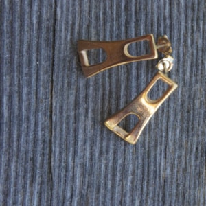 May include: A pair of gold-toned earrings with a geometric design. The earrings are shaped like a rectangle with a smaller rectangle cut out of the center.