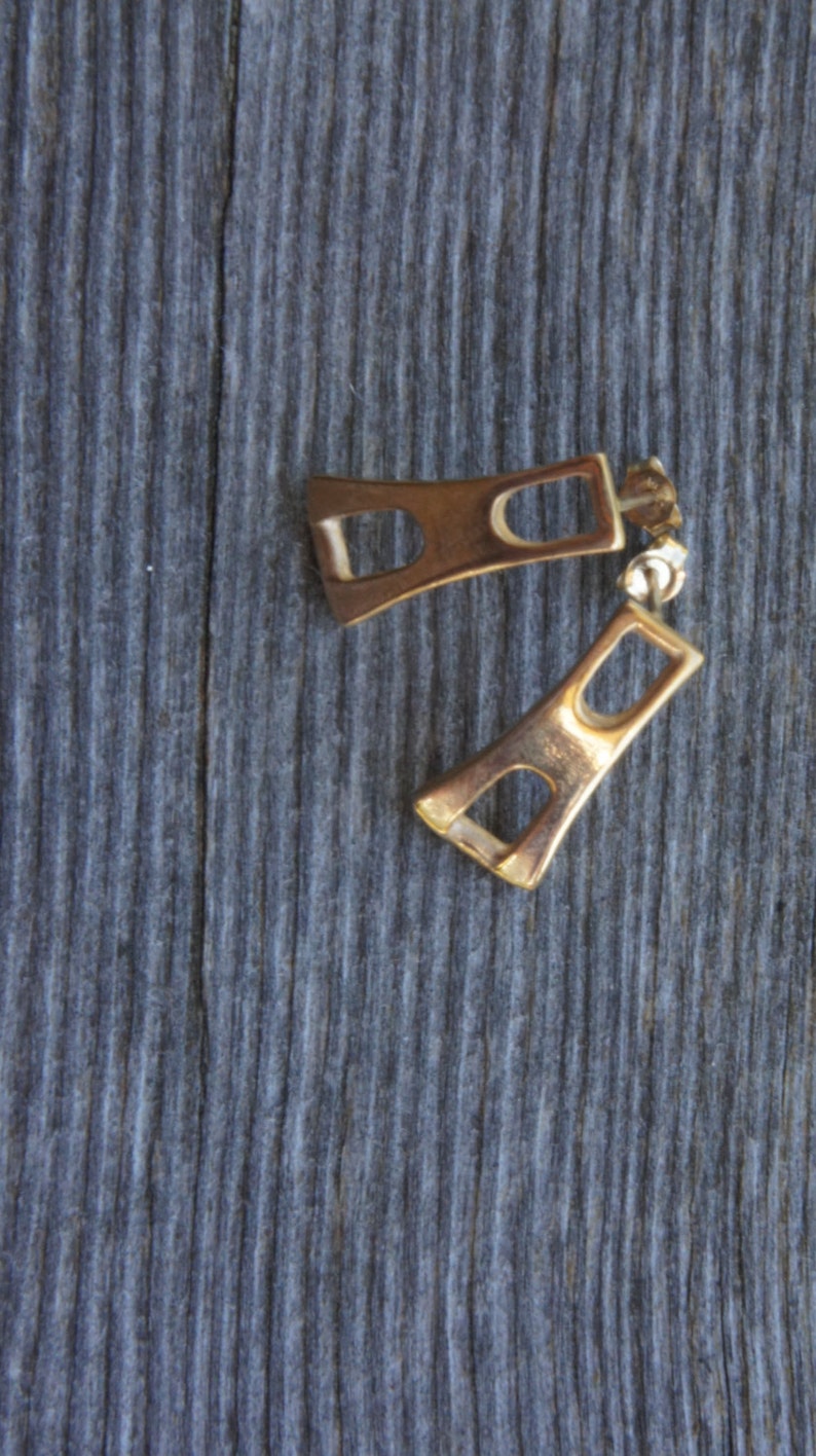 May include: A pair of gold-toned earrings with a geometric design. The earrings are shaped like a rectangle with a smaller rectangle cut out of the center.