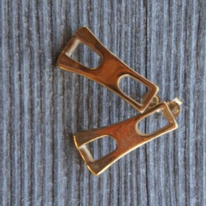 May include: A pair of gold-toned geometric earrings with a rectangular shape and a cutout design.