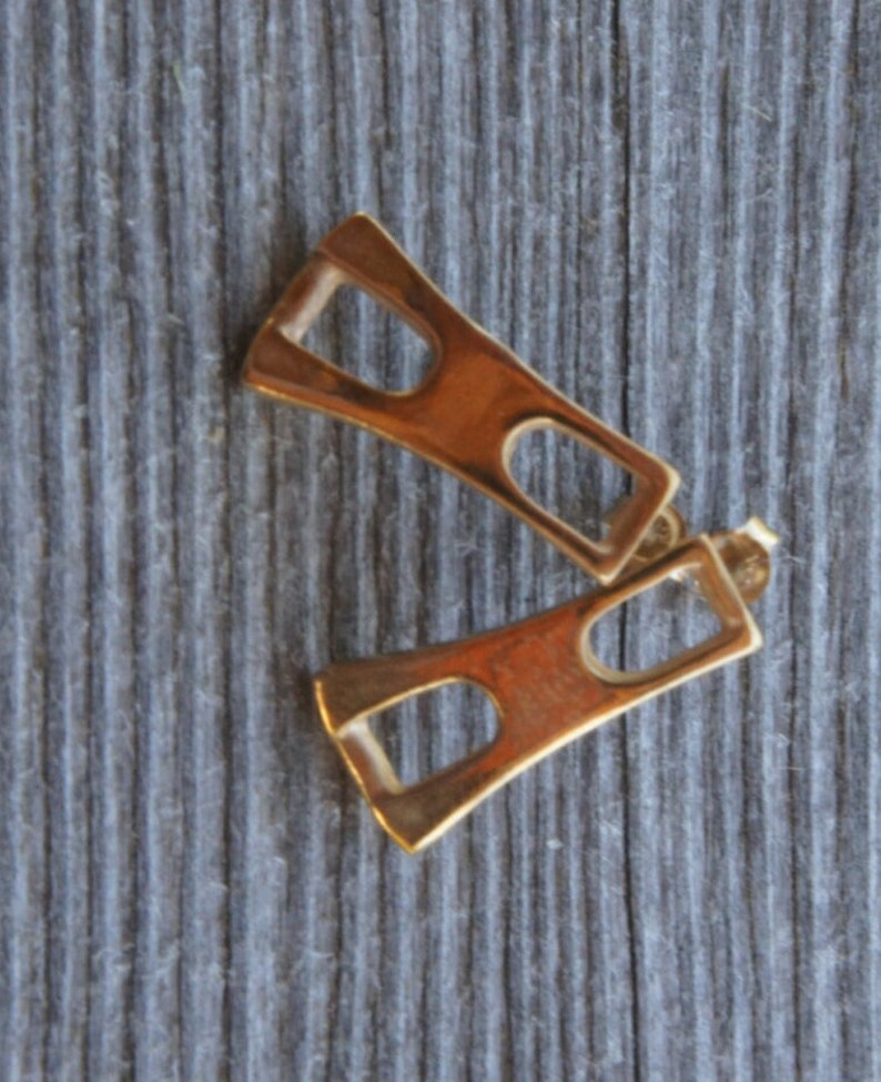May include: A pair of gold-toned geometric earrings with a rectangular shape and a cutout design.