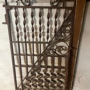 May include: A rusty metal gate with a decorative design. The gate is made of wrought iron and has a geometric pattern. The gate is in need of a paint job.