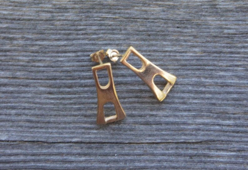 May include: A pair of gold-toned earrings with a geometric design. The earrings are shaped like a rectangle with a cut-out in the center.