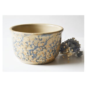Puede incluir: Un tazón de mezcla de cerámica vintage de color crema con un glaseado moteado azul y marrón.