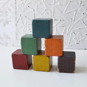 Peut inclure: Une pyramide de sept blocs de bois colorés. Les blocs sont dans des tons de bleu-vert, vert, orange, rouge, jaune et marron. Les blocs sont disposés en forme de pyramide, mettant en valeur leurs couleurs vives et leur design simple.