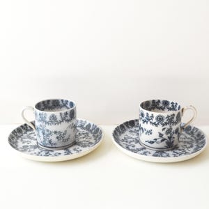 May include: Two matching porcelain teacups and saucers. The cups and saucers are white with a blue floral pattern. The cups have small handles and sit on round saucers. The set is ideal for serving tea or coffee.