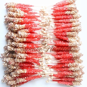 May include: A bunch of red and gold rock candy sticks on wooden sticks. The candy is arranged in a fan shape.