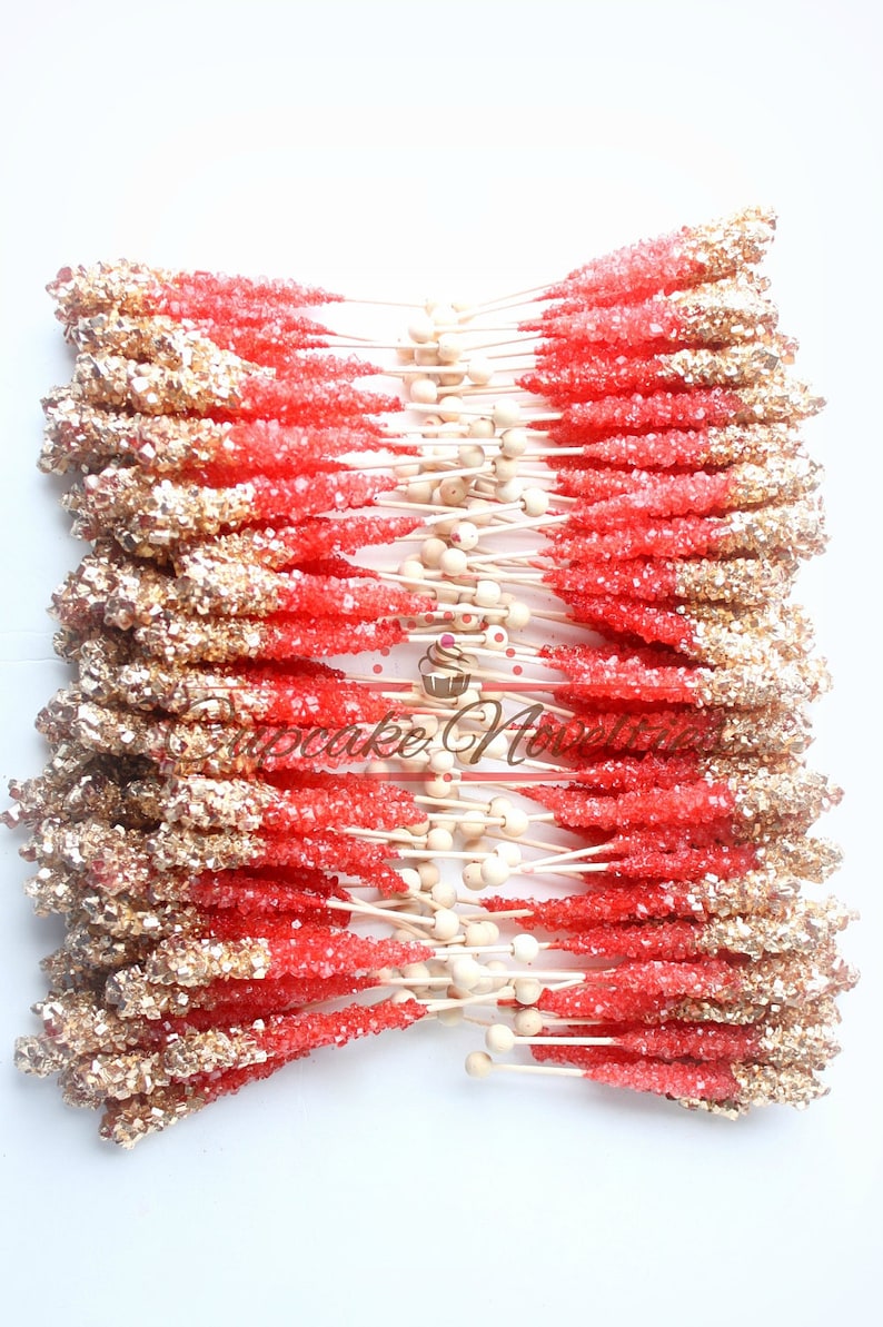 May include: A bunch of red and gold rock candy sticks on wooden sticks. The candy is arranged in a fan shape.