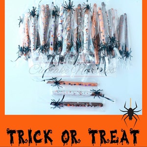 May include: A collection of chocolate-covered pretzel sticks decorated with Halloween-themed sprinkles and black spider accents. The pretzel sticks are individually wrapped in clear cellophane bags and arranged on a white surface. The text "TRICK OR TREAT" is written in black dripping letters on an orange background.