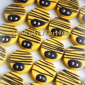 May include: A collection of yellow and black bee-themed chocolate covered Oreos. The Oreos are decorated with black stripes and two black googly eyes.
