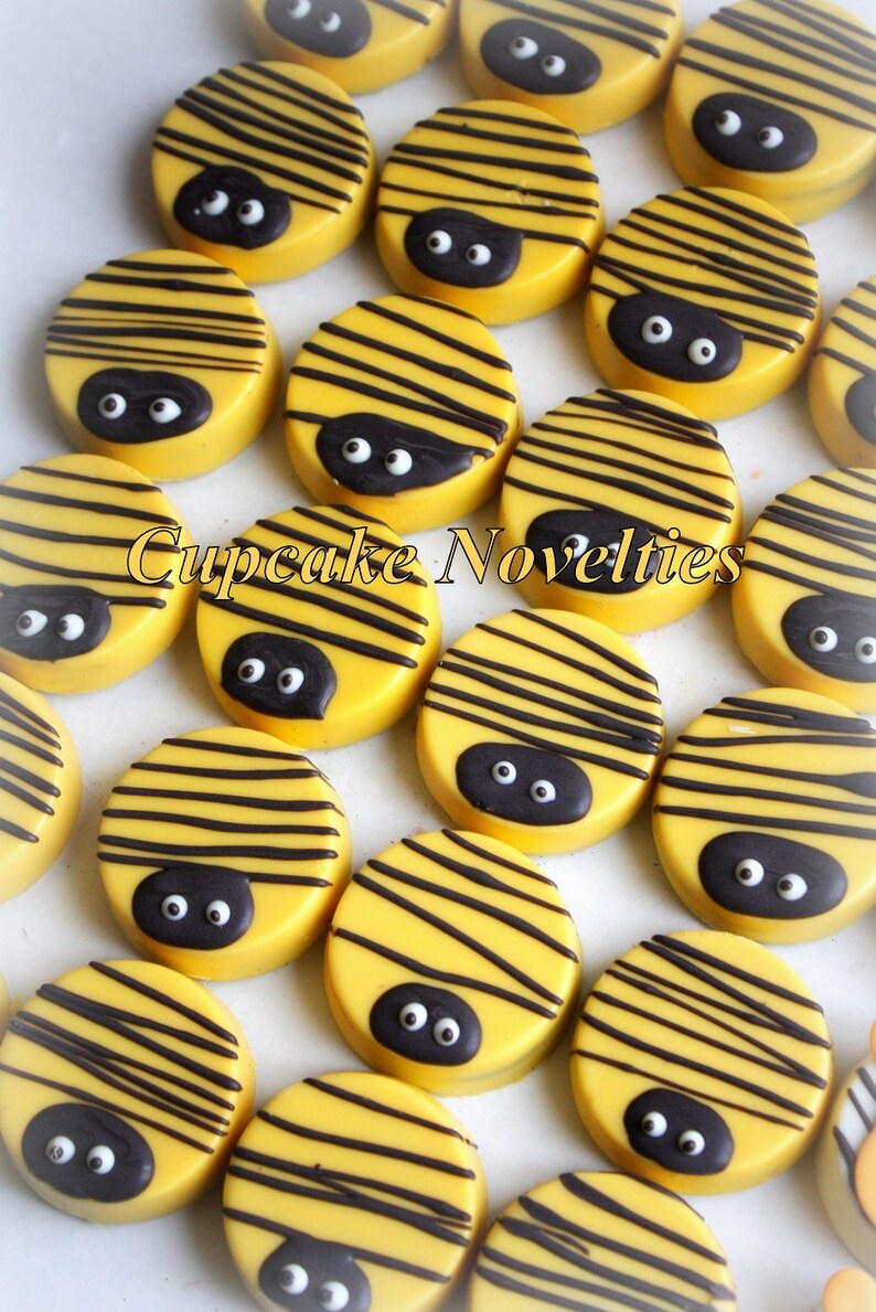 May include: A collection of yellow and black bee-themed chocolate covered Oreos. The Oreos are decorated with black stripes and two black googly eyes.