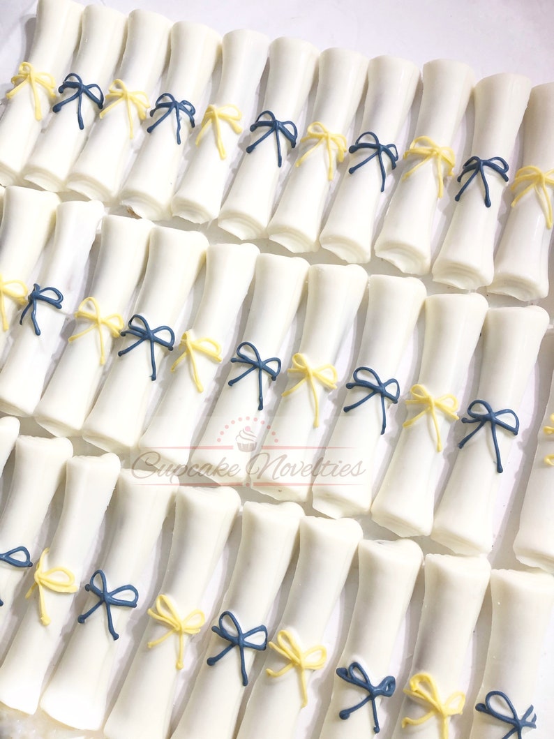 May include: White chocolate graduation cap shaped treats decorated with blue and yellow bows. Cupcake Novelties.