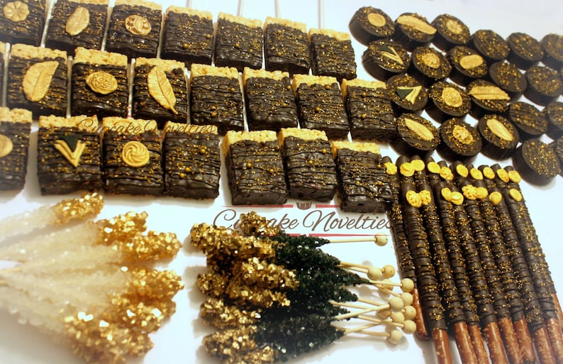 May include: Assortment of black and gold chocolate-covered treats, including rice krispie treats, pretzel sticks, and chocolate-covered pretzels. The treats are arranged on a white surface with gold and black sprinkles.
