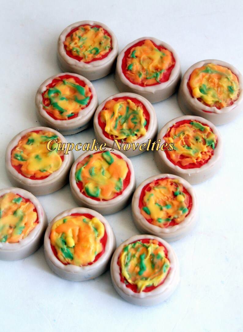 May include: A collection of 10 mini pizza cupcakes decorated with red, yellow, and green frosting. The cupcakes are arranged in a circle on a white surface. Cupcake Novelties is written in gold letters on the image.