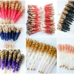 May include: Assortment of colorful rock candy sticks with gold glitter on top. The candy sticks are arranged in groups of different colors, including pink, blue, purple, and white. Each stick is attached to a wooden stick with a round wooden bead at the end.