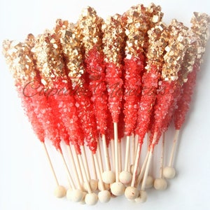 May include: A bunch of red and gold rock candy sticks on wooden sticks with round wooden ends.