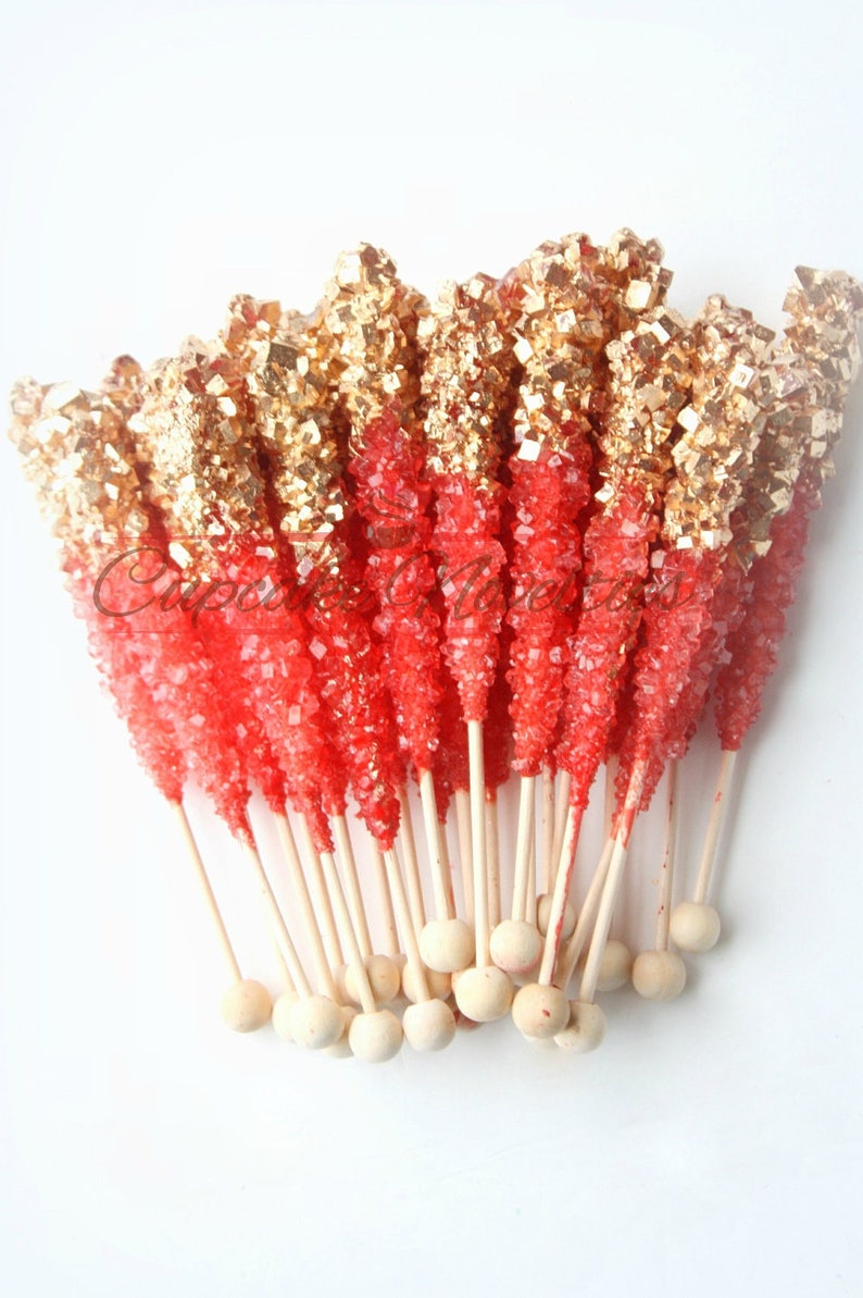 May include: A bunch of red and gold rock candy sticks on wooden sticks with round wooden ends.