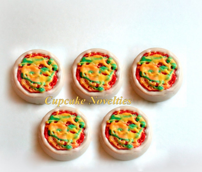 May include: Five mini pizza cupcakes decorated with red, yellow, and green frosting. The cupcakes are arranged in a circle on a white surface. Cupcake Novelties is written in the center of the image.