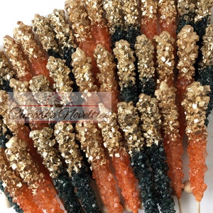 May include: A bunch of orange and green rock candy sticks with gold glitter on top. The candy sticks are on wooden sticks and are arranged in a fan shape.