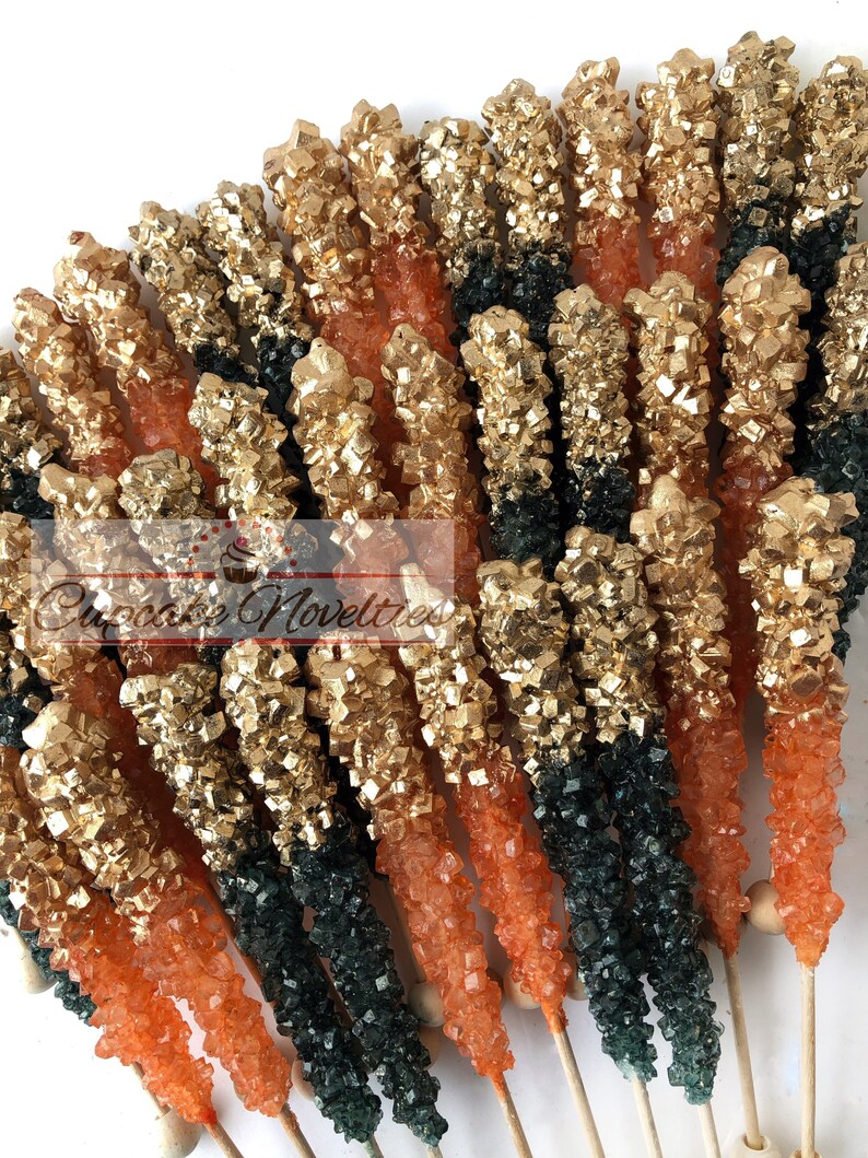 May include: A bunch of orange and green rock candy sticks with gold glitter on top. The candy sticks are on wooden sticks and are arranged in a fan shape.