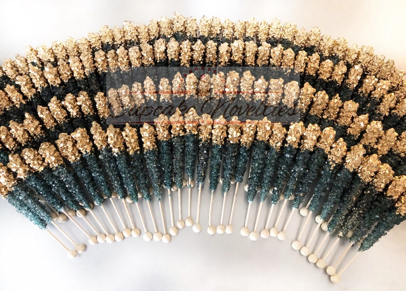 May include: A large group of gold and teal rock candy sticks on white sticks. The candy is arranged in a semi-circle shape.