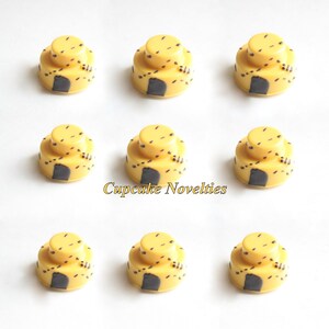 May include: Nine yellow and black cupcake toppers shaped like beehives. The toppers are decorated with black dots and a black door.