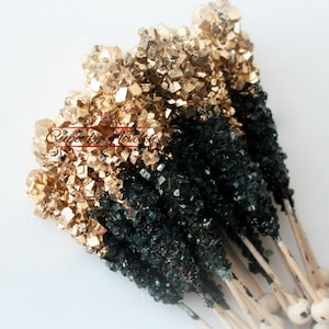 May include: A bunch of black and gold rock candy sticks on wooden sticks. The candy is in the shape of crystals.